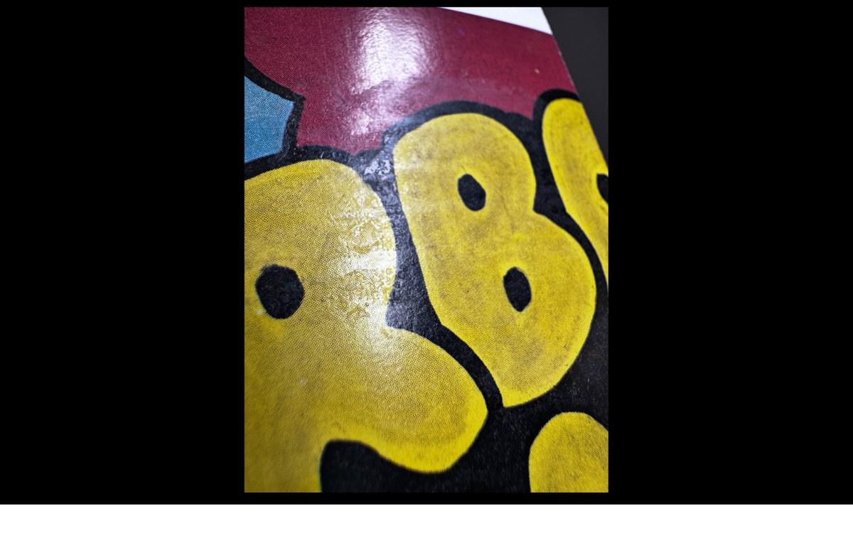 Macro photograph of the back of a 1989 OPC Wacky card showing part of a puzzle piece, with a translucent wax film catching the light at an angle across the printed yellow and red ink.